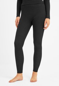 Woman wearing fitted black ribbed leggings and matching long-sleeve top, standing barefoot against a plain white background.