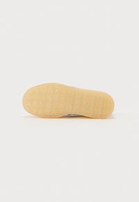 Såle av en sneakers med gummimateriale, gjennomsiktig gul farge, strukturert gripe mønster og rund hælform.