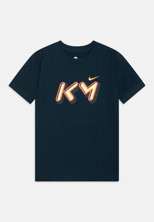 Marineblauw Nike T-shirt met korte mouwen met gestileerde "KY" tekst in perzik en geel, met een kleine oranje Nike swoosh boven de letters.