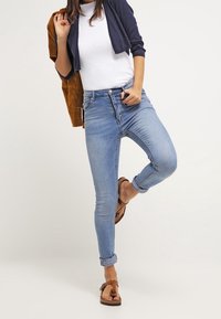 Smala blå jeans med en urtvättad look, hög midja, upprullade fållar, kompletterade med en vit t-shirt och en mörk cardigan. Bruna sandaler.