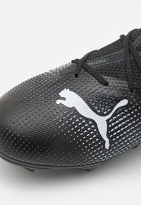 Scarpa da calcio nera con tomaia testurizzata, caratterizzata da un prominente logo Puma bianco e lacci neri. Progettata per trazione e supporto su superfici erbose.