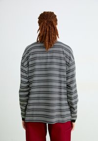 Camicia a maniche lunghe con strisce orizzontali bianche e nere, caratterizzata da una vestibilità comoda e polsini a coste, abbinata a pantaloni bordeaux.