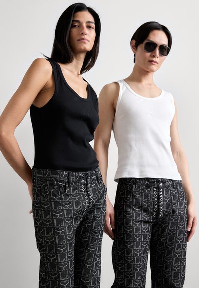 Des débardeurs noir et blanc associés à des pantalons taille haute à motifs avec un devant lacé. Les débardeurs ont une coupe ajustée et une marque subtile.