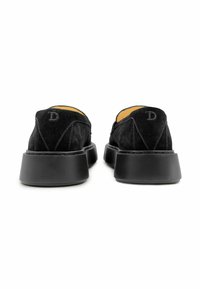 Zwarte suède schoenen met een platte rubberen zool, voorzien van een afgeronde achterkant, gestikte details en een kleine geperste 'D' op de achterkant.