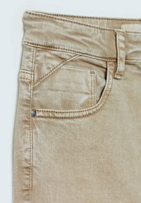 Pantalones de denim beige con cinco bolsillos, que incluyen un bolsillo frontal para monedas, acabados con costuras en contraste y un pequeño detalle de remache metálico.