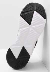 Svart och vit sportskosula med geometriskt mönster; texturerad svart gummihäl och vit mellansula för grepp och hållbarhet.