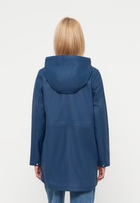 Στεγανό αδιάβροχο μπουφάν ναυτικού μπλε με κουκούλα, με λεία υφή και ευθύ κομψό σχέδιο. Η πίσω όψη δείχνει απλό σχέδιο χωρίς διακοσμήσεις.