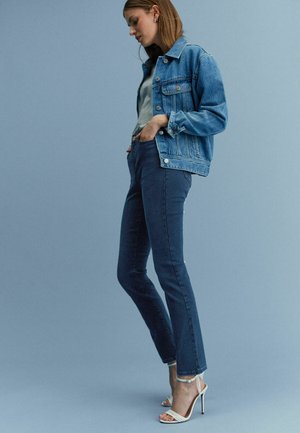 Heled sinise denim-jakk, millel on rinna taskud, ja tumedama sinise slim-fit püksid, millel on kerge fläär, mis on lisatud valgete kontsadega.