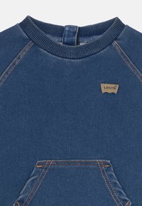 Blå denimtröja med ribbad halsringning, framficka med kenguru-design, orange sömmar och en liten brun Levi's logotypapplikation på bröstet.
