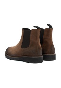 Botine Chelsea din suede maro, cu panouri elastice pe laturile laterale, munchii de tragere și o talpă groasă din cauciuc negru. Textură netedă și design minimalist.