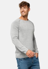 Gråstribet sweater lavet af tekstureret strikstof med lange ærmer og ribbet manchetter, båret med blå jeans.
