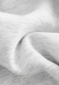 Bawełniana tkanina w jasnoszarym kolorze, o gładkiej fakturze z delikatnymi nieregularnościami i zagnieceniami, podkreślająca jej miękkość i zdolność do układania się.