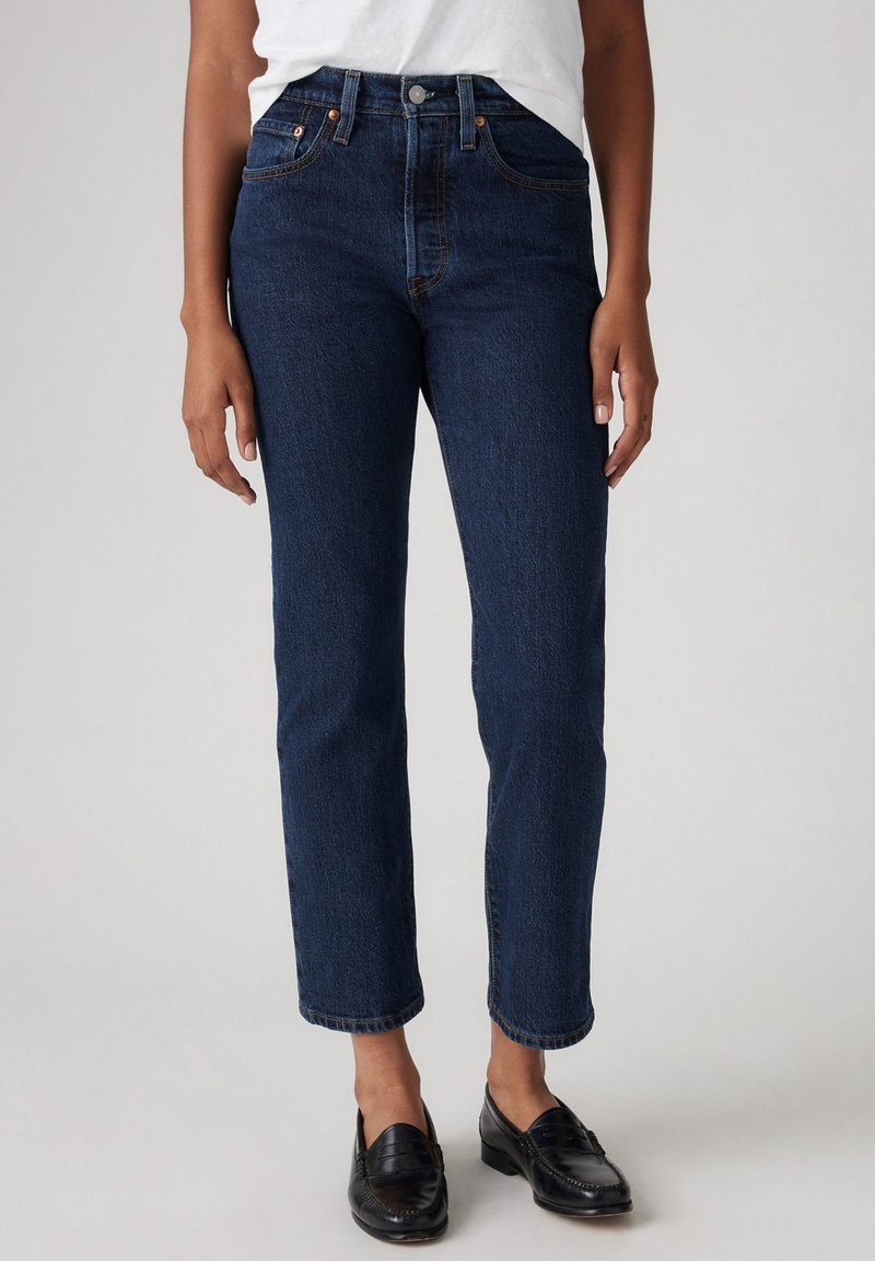 Tumed sinised denim püksid, kõrge talje ja sirge jala designiga, kahe esipocketiga ja vasktoodete aktsentidega. Ilma nähtavate mustritega.