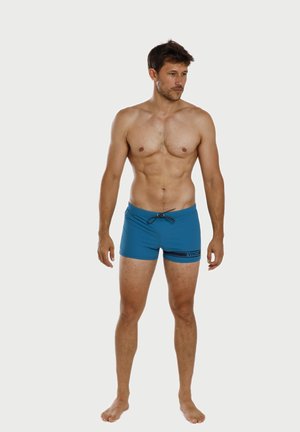 Blue swim shorts made of stretchy fabric, featuring an elastic waistband with a drawstring and a small black logo on the front.