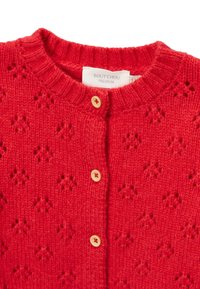 Cardigan en tricot rouge avec un col rond, présentant un motif intégral et deux boutons en bois sur le devant. Étiquette indiquant "BOUT CHOU PREMIUM."