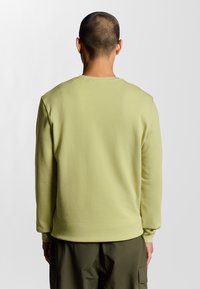 Felpa gialla chiaro con maniche lunghe, colletto e polsini a coste. Tessuto morbido, vestibilità rilassata, abbinata a pantaloni verde scuro.
