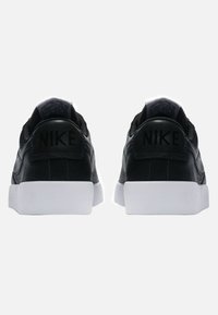Zapatillas de cuero negro con suelas de goma blanca, presentando un logo de Nike negro en el talón y una textura suave.