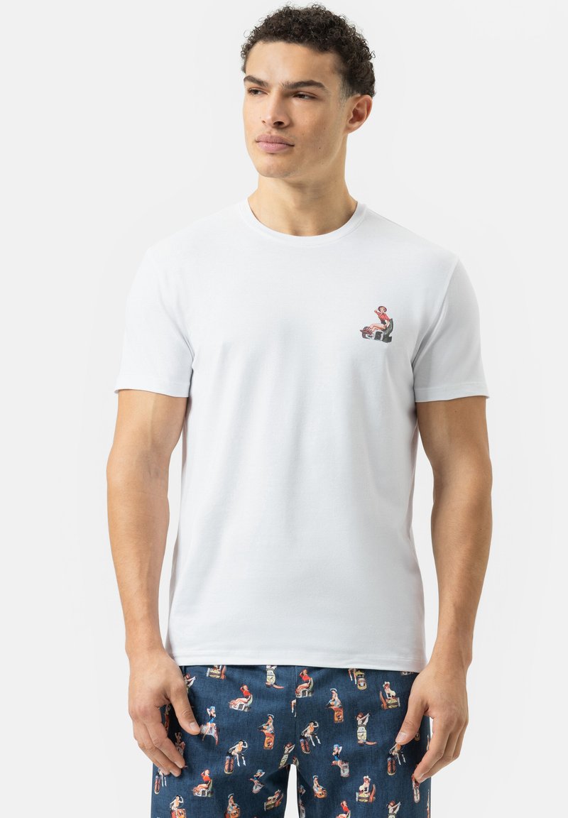 Witte katoenen t-shirt met een kleine grafische print op de linkerkant van de borst. Gecombineerd met marineblauwe broek met kleurrijke patronen van vintage-figuren.