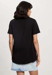 Czarna bawełniana koszulka z krótkim rękawem, okrągłym dekoltem i luźnym krojem, zestawiona z jasnoniebieską mini spódnicą dżinsową. Bez wyraźnych wzorów czy elementów metalowych.