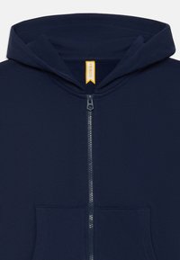 Felpa con zip di colore blu navy realizzata in un tessuto morbido, dotata di una tasca frontale e di un cappuccio con un'etichetta gialla che riporta la scritta "FRIBOO". Cerniera liscia.
