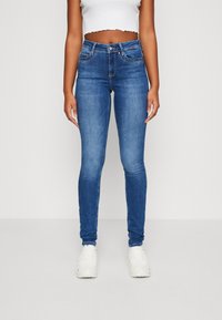 Tynne blå jeans laget av denim med en glatt tekstur, fem-lomme design og glidelås åpning. Brukt med hvite sneakers.