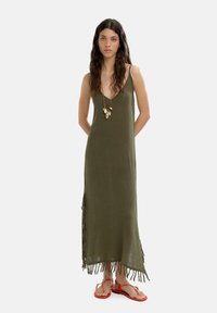 Olivejgreenowa sukienka maxi z spaghetti straps, z frędzlami na dole, połączona z czerwonymi klapkami i naszyjnikiem z warstwami.