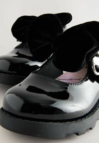 Schwarze lacklederschuhe mit Samtbögen, abgerundeter Zehenpartie und strukturiertem Sohlen. Verfügt über ein elastisches Band für einen sicheren Sitz. Weiche Innenauskleidung.