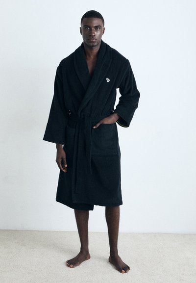 Robe en coton noir avec col châle, dotée d'une ceinture à nouer, de deux poches avant et d'un petit logo sur la poitrine. Tissu texturé.