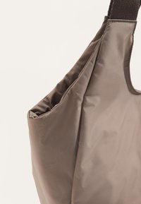 Barna nejlon táska puha, sima textúrával, laza kialakítással és széles vállpánttal. Egyszerű és minimalista stílus.