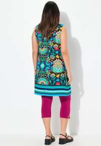 Tunika colorata con motivo su sfondo nero, disegni floreali blu, arancioni e verdi, abbinata a leggings a tre quarti magenta e sandali neri.