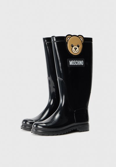 Bottes de pluie en caoutchouc noir avec une texture lisse, une pointe arrondie et un accent en forme d'ours. Présente un logo Moschino sur le côté.