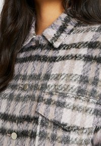 Checked wool jacket featuring a collar, metallic buttons, and a front pocket with varying shades of purple, gray, and black in a soft texture.