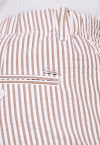 Gestreepte broek in wit en lichtbruin met een gestructureerde stof. Bevat een verticaal streeppatroon en een klein metalen logo op de zak.