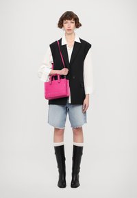 Borsa a tracolla con trama di coccodrillo rosa, dotata di manici doppi e tracolla, abbinata a un gilet nero, una camicia bianca, pantaloni shorts in denim e stivali neri.