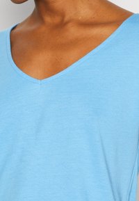 Světle modrý top s krátkým rukávem a výstřihem do V. Vyroben z měkké a hladké tkaniny, s pohodlným střihem a jemnou texturou.
