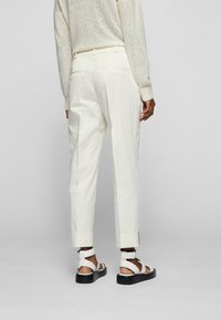 Kremowe, dopasowane spodnie o prostym kroju, z mankietami u dołu i dwiema tylnymi kieszeniami, zestawione z białymi sandałami na czarnym, teksturowanym spodzie.