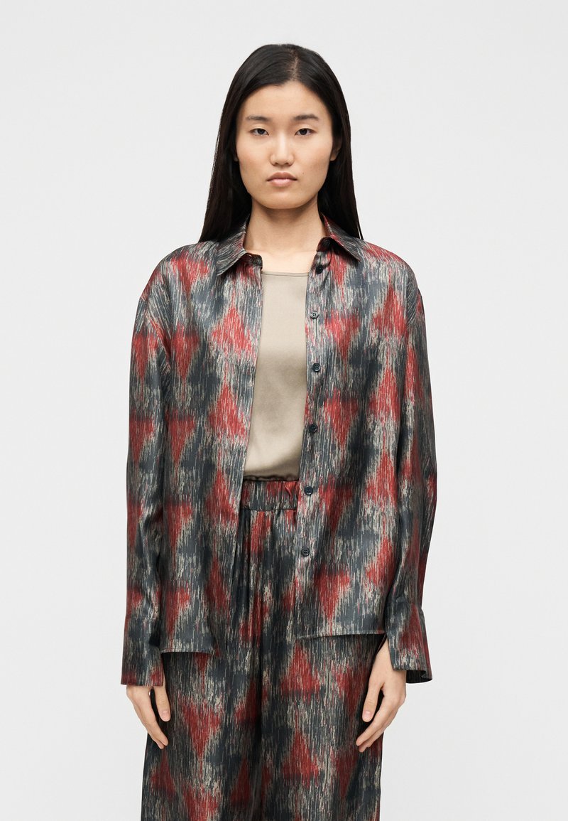 Trykt skjorte og matchende bukser i mørke nuancer med røde og grå mønstre. Glat, letvægtsstof med krave og knapper.