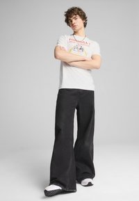 Hvid t-shirt med et rødt og gult "Formula 1" grafik, parret med vide sorte jeans og hvide sneakers med sorte såler.