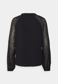 Blouse noire avec dos uni et manches longues transparentes présentant un motif chevron et des poignets froncés.