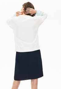 Felpa bianca con colletto rotondo e maniche lunghe, abbinata a una gonna blu navy. Il materiale sembra liscio con una vestibilità comoda.