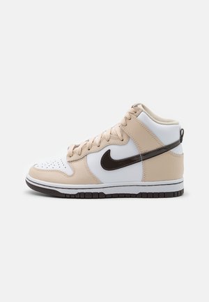 Wysokie sneakersy z białej i beżowej skóry z czarnym logo Nike, beżowymi sznurówkami i czarno-białą gumową podeszwą, widok z boku na jednolitym tle.