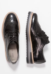 Chaussures en cuir verni noir avec détails en brogue, bout rond, semelle plate et lacets. Présente une semelle texturée et contrastante.