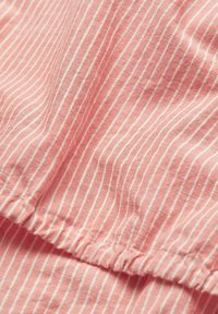 Tessuto leggero rosa con strisce verticali bianche, caratterizzato da una cucitura arricciata nella parte inferiore. Texture morbida con una caduta informale.