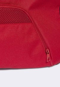 Borsa in tessuto rosso con superficie testurizzata, dotata di una tasca laterale in rete e chiusura con zip dello stesso colore. Design resistente per l'uso quotidiano.