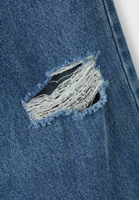 Tessuto in denim strappato con un grande strappo sfilacciato che espone fili bianchi. Sfondo blu con diverse sfumature di blu e texture.