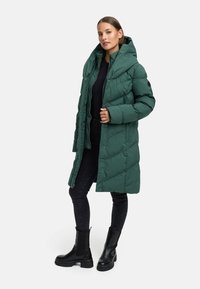 Grön puffjacka med hög krage och knappar, med en quiltad textur. Bärs över svarta jeans och svarta ankelskor.