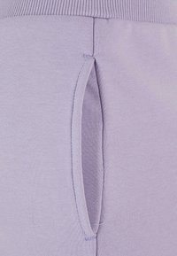 Lilafarget joggebukser med ribbestrikket midje, en sidelomme og en glatt, myk tekstur. Stoffet er lett og elastisk.