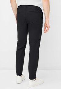 Zwarte broek van een gladde stof, met een slim fit, twee achterzakken en een strak ontwerp zonder zichtbare logo's. Gecombineerd met witte sneakers.