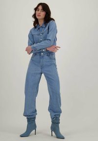 Lichtblauwe denimoutfit met een knoopjack en hoog-getailleerde broeken, gecombineerd met lichtblauwe, slungelige haklaarzen.