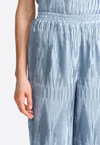 Light blue pleated trousers made of satin fabric, featuring an elastic waistband, nuanced texture, and vertical stripes enhancing the design.